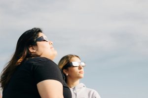 Two women viewing the solar eclipse using specialized eclipse glasses.